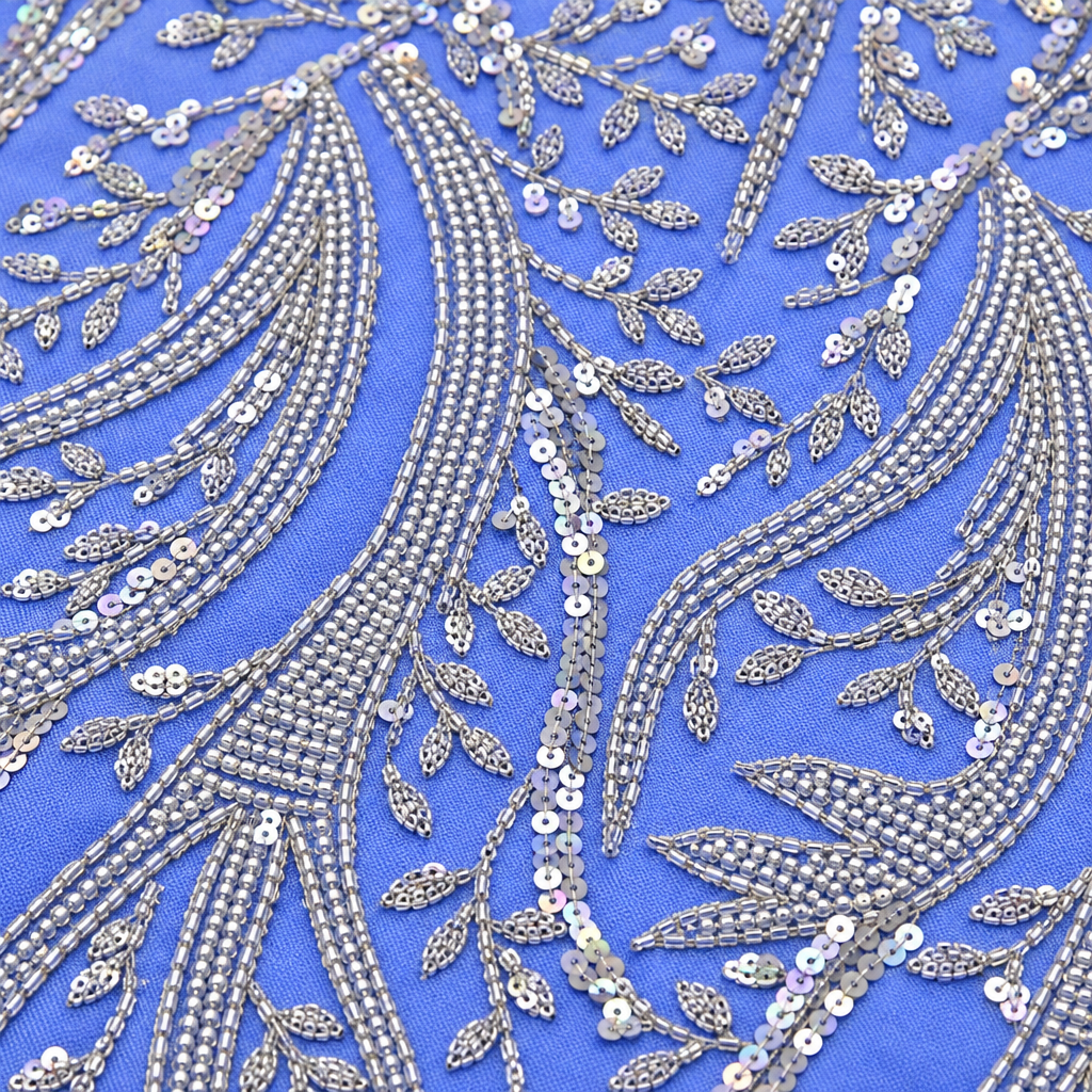Close-up of silver bead and sequin feather embroidery on periwinkle blue fabric